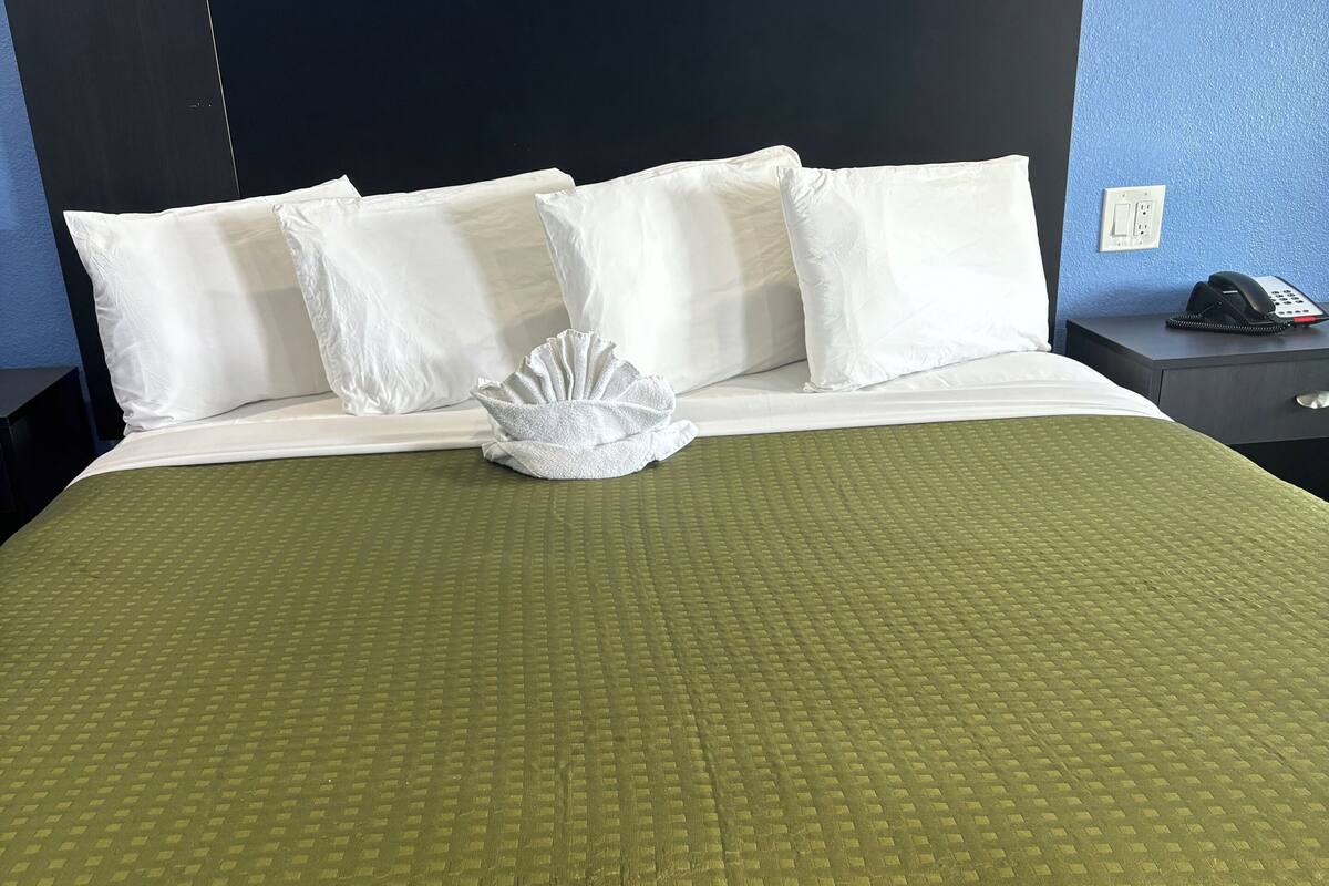A neatly made bed with a green quilt, white pillows, and a white decorative item on the bed.