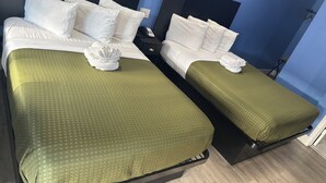 Ein Hotelzimmer mit zwei Betten, jeweils mit weißer Bettwäsche und grünen Decken. Es gibt zwei Nachttische mit Lampen und einem Telefon.
