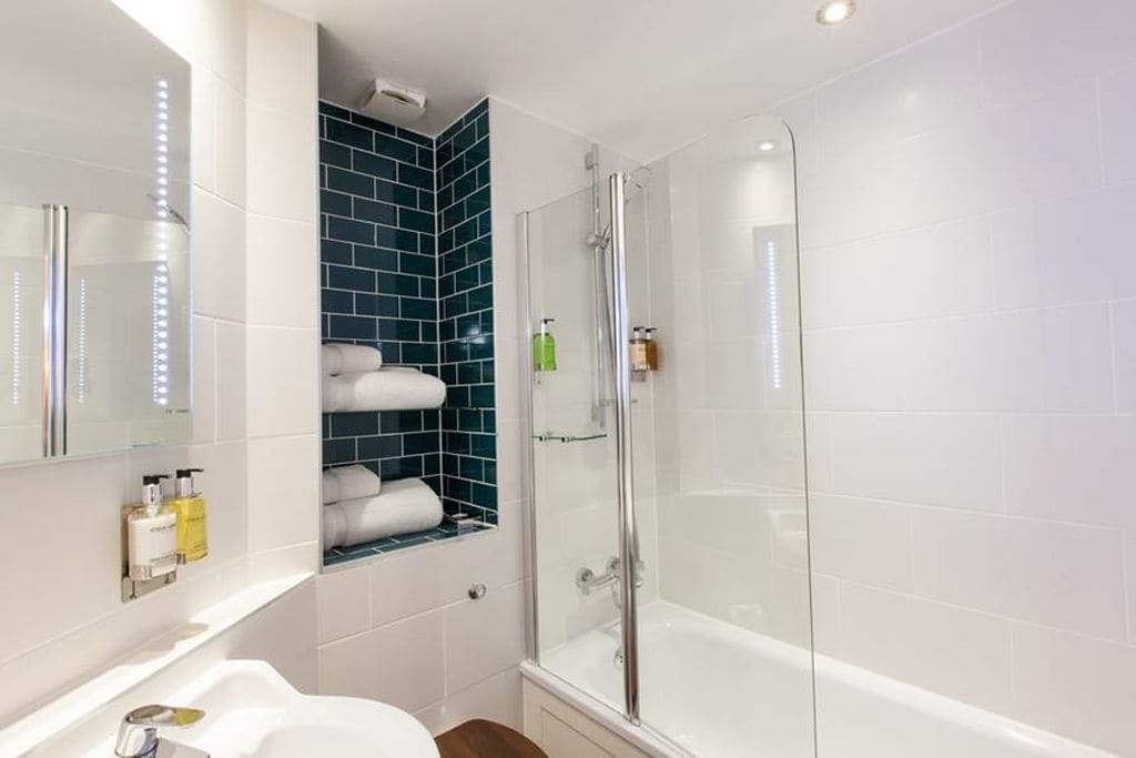 A modern bathroom with a glass-enclosed shower, white tiles, and a blue accent wall.