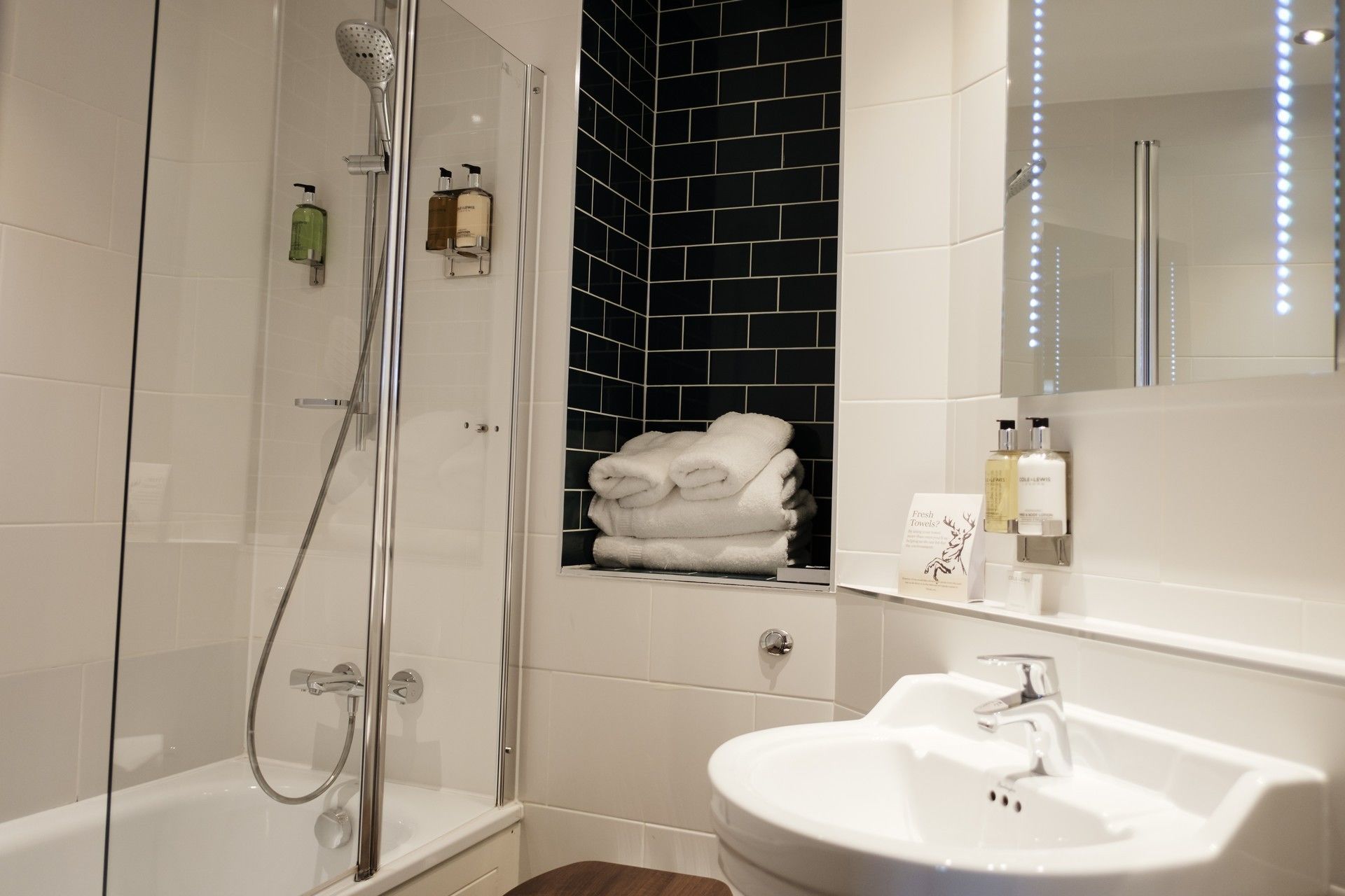 A modern bathroom with a glass-enclosed shower, a white sink, and a towel rack with folded towels.