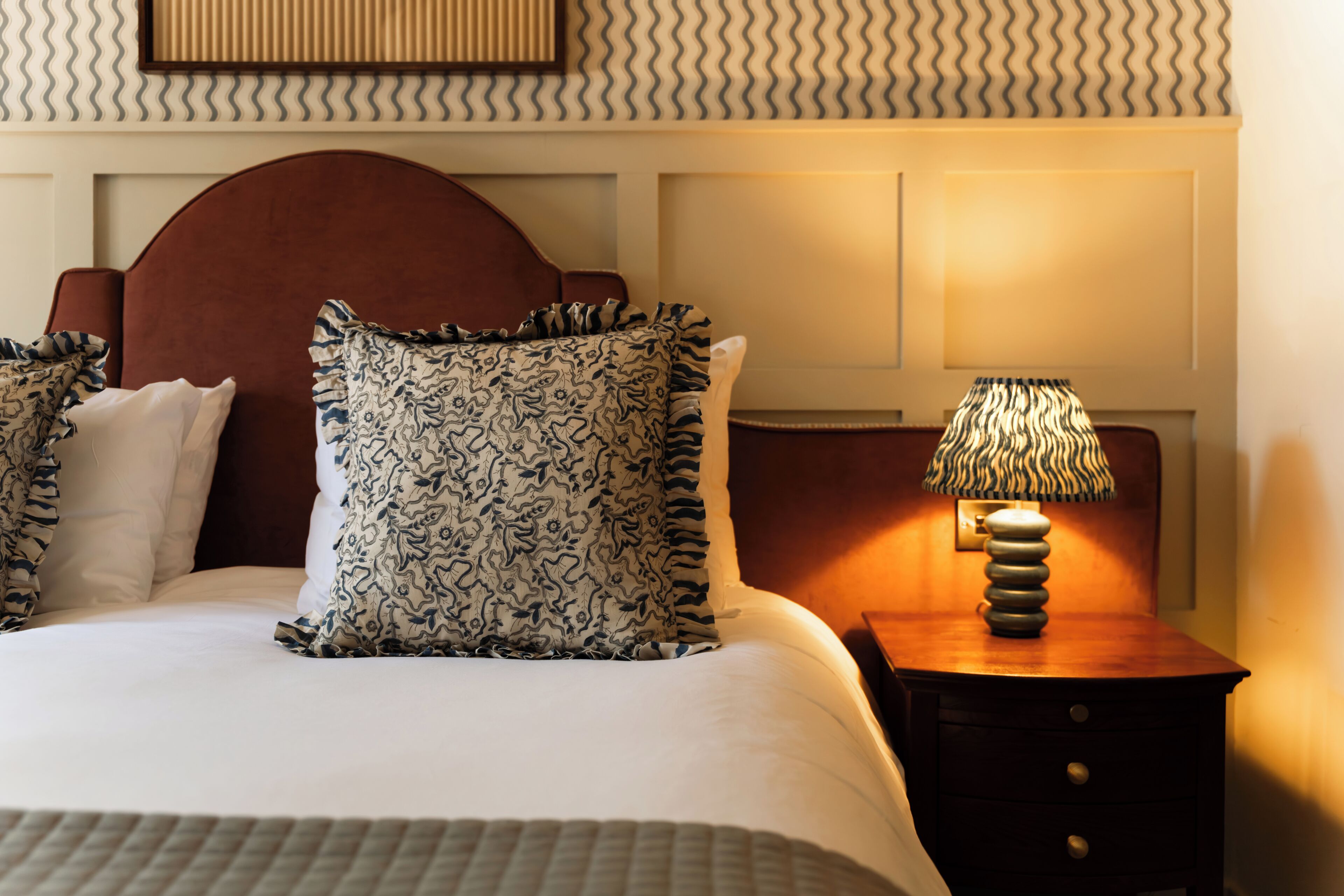 A neatly made bed with patterned pillows, a wooden headboard, and a bedside table with a lamp.