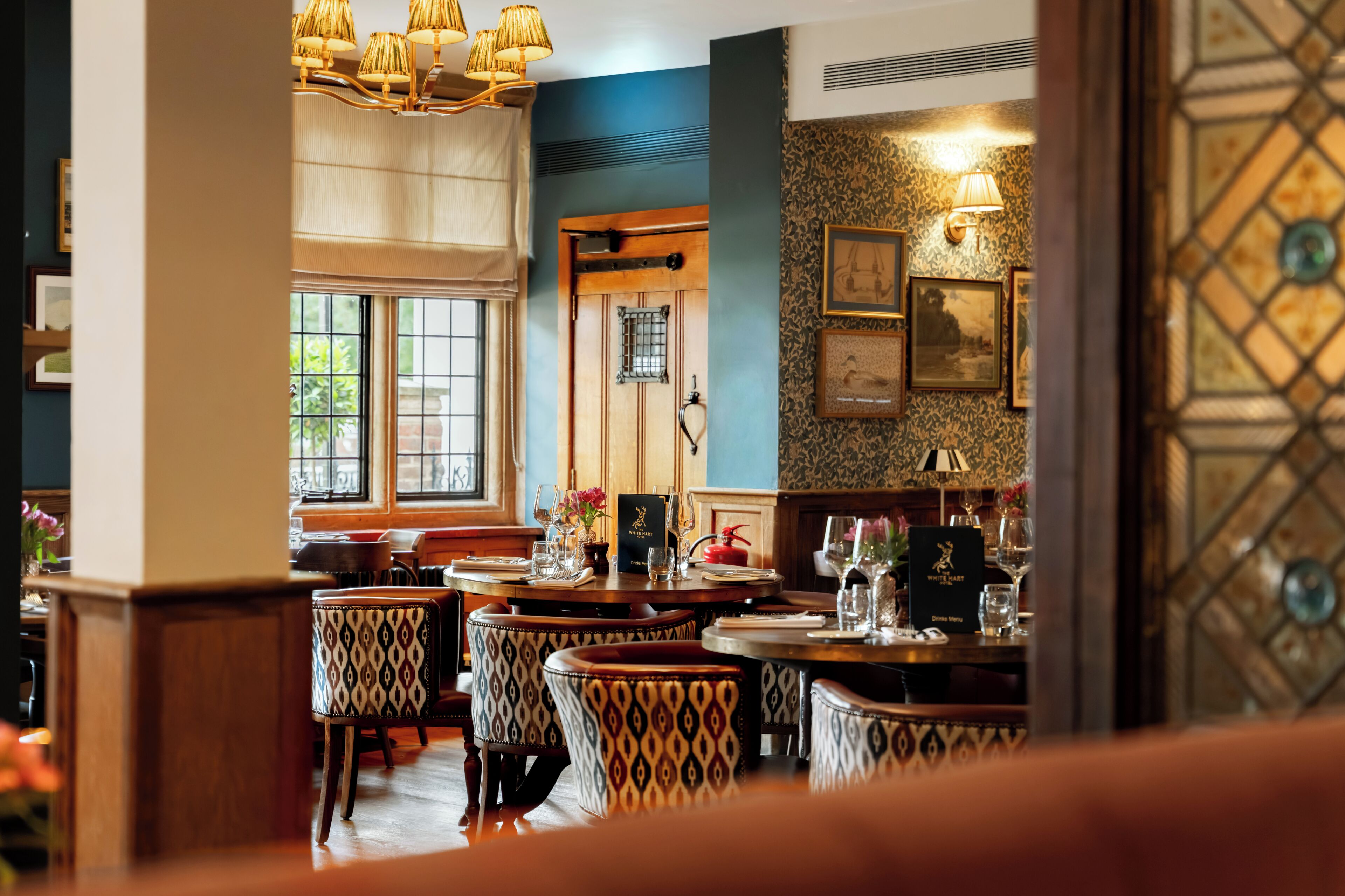 A restaurant interior with wooden tables, patterned chairs, and a blue accent wall.