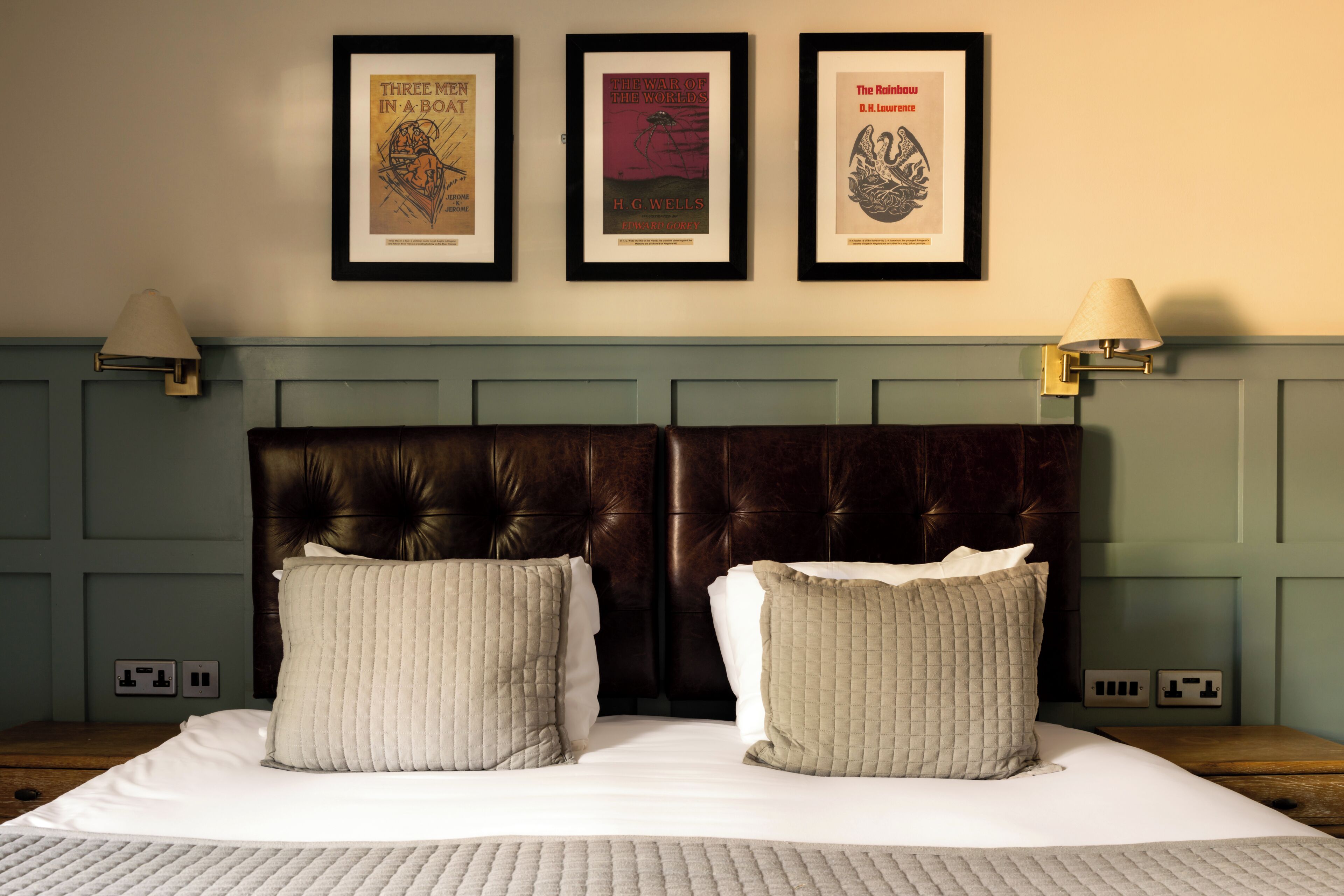 A neatly made bed with two pillows, a headboard, and three framed books on the wall above.