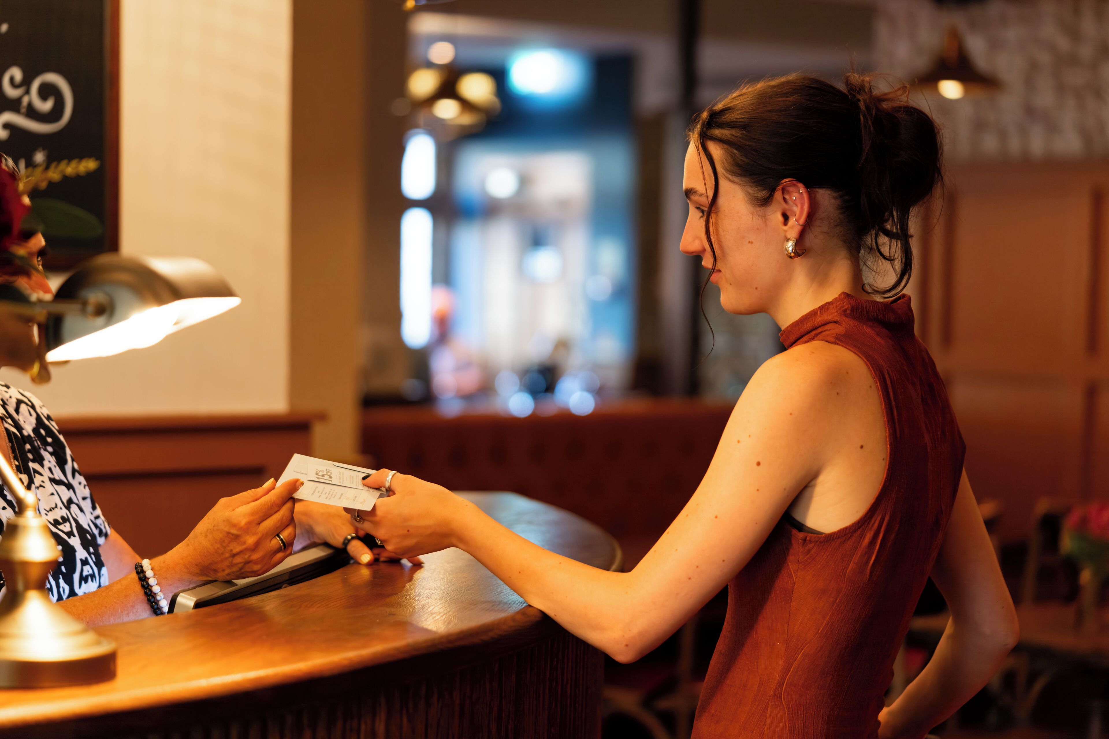 Une personne se tient derrière un comptoir, peut-être à la réception d’un hôtel, et elle a une carte et un stylo à portée de main.