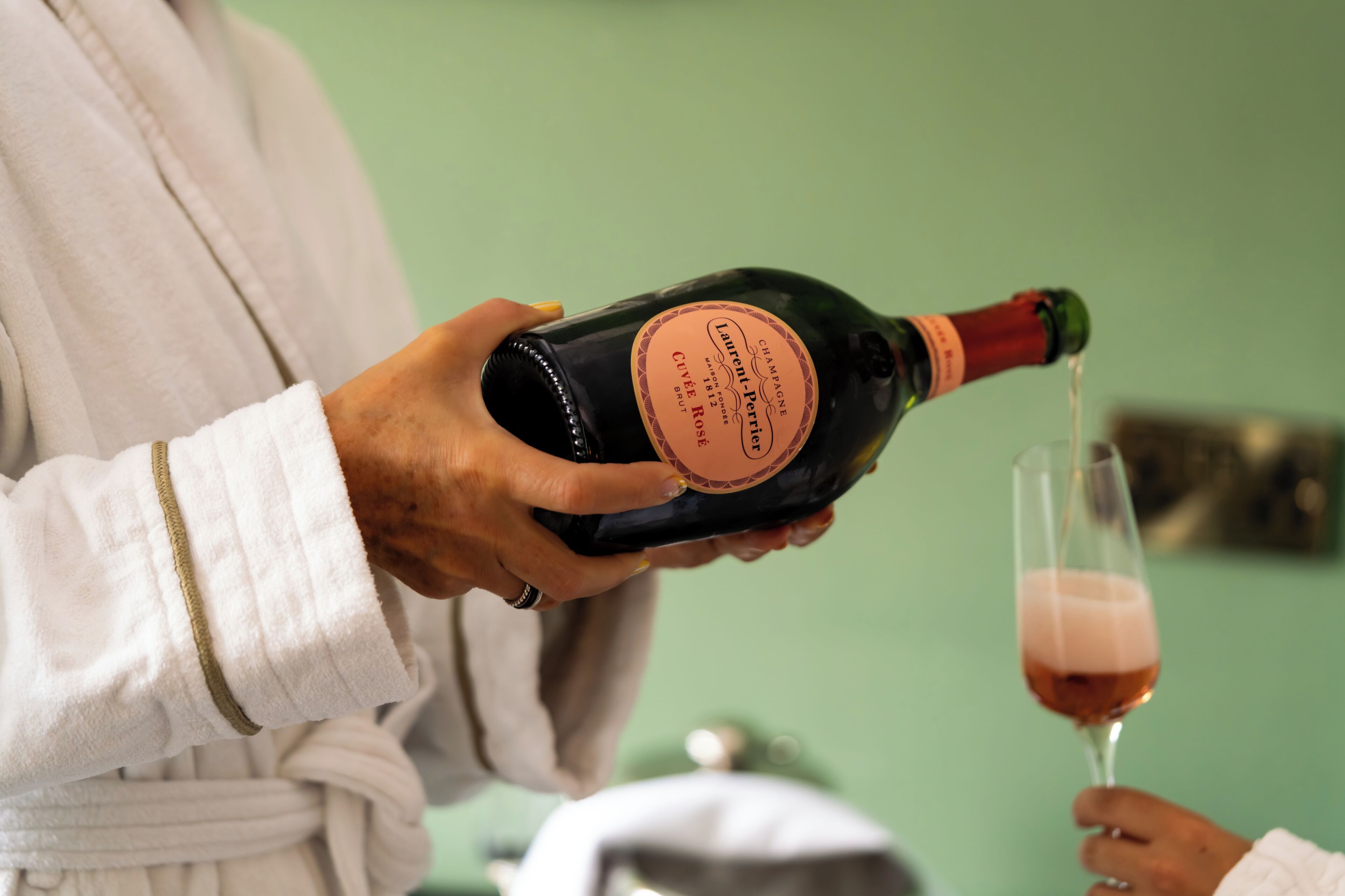 A person holding a bottle of champagne, with a glass of champagne being poured.