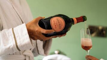 A person holding a bottle of champagne, with a glass of champagne being poured.