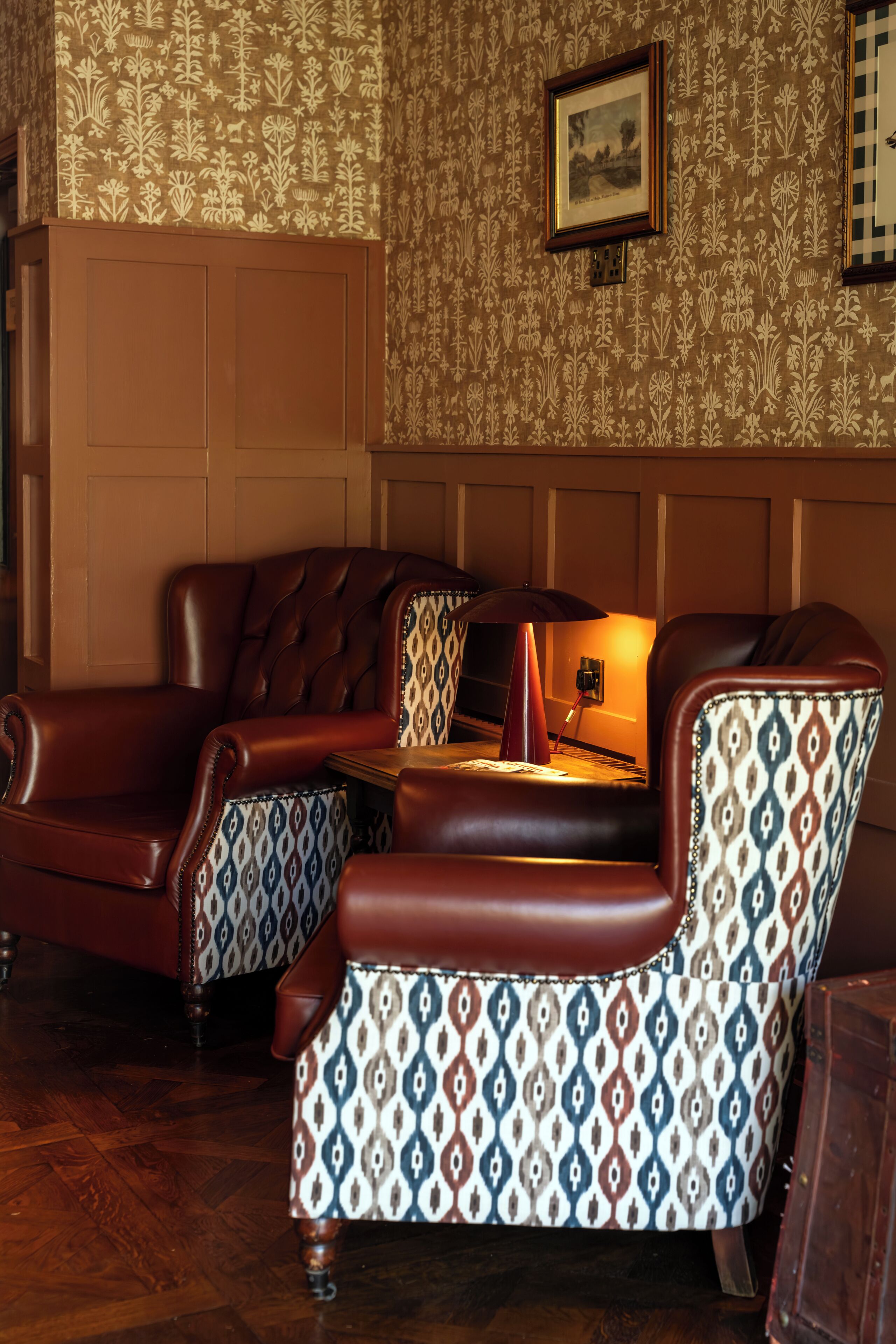 A room with a brown leather sofa, patterned armchairs, and a wooden table.