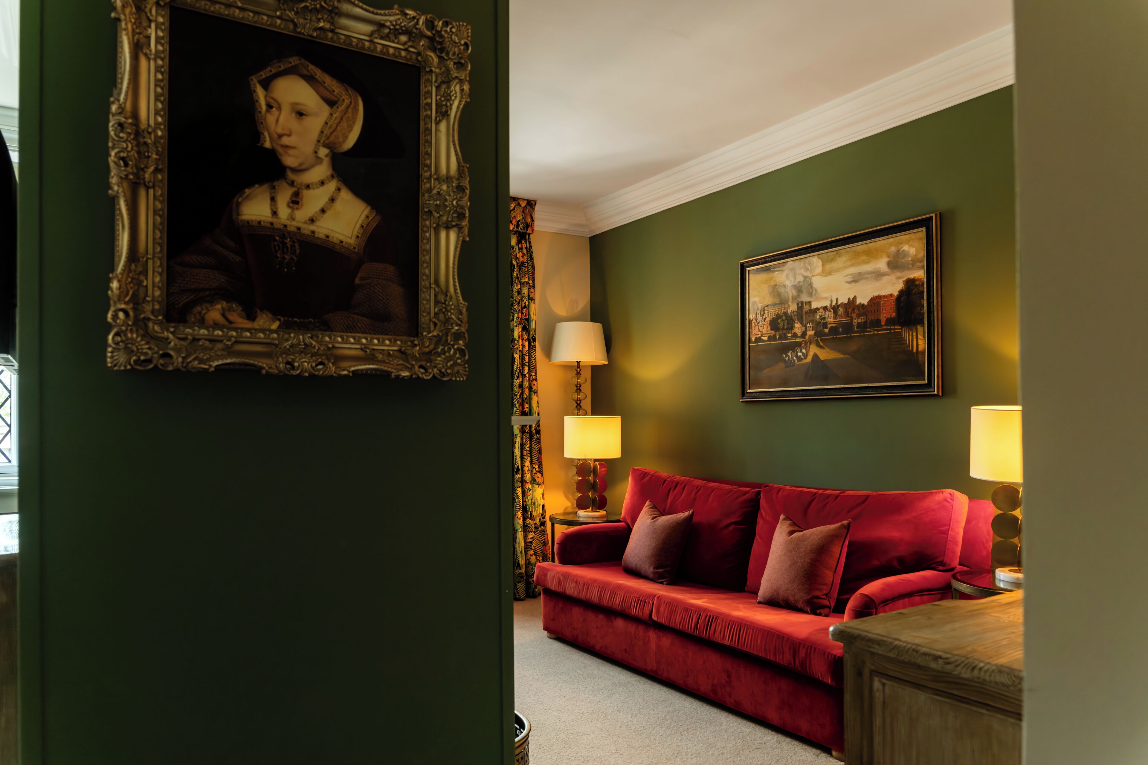 Een kamer met een rode bank, een lijst met portret en een landschap op de muur.