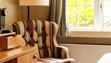 A hotel room with a bed, a desk with a lamp, a striped armchair, and a window with curtains.