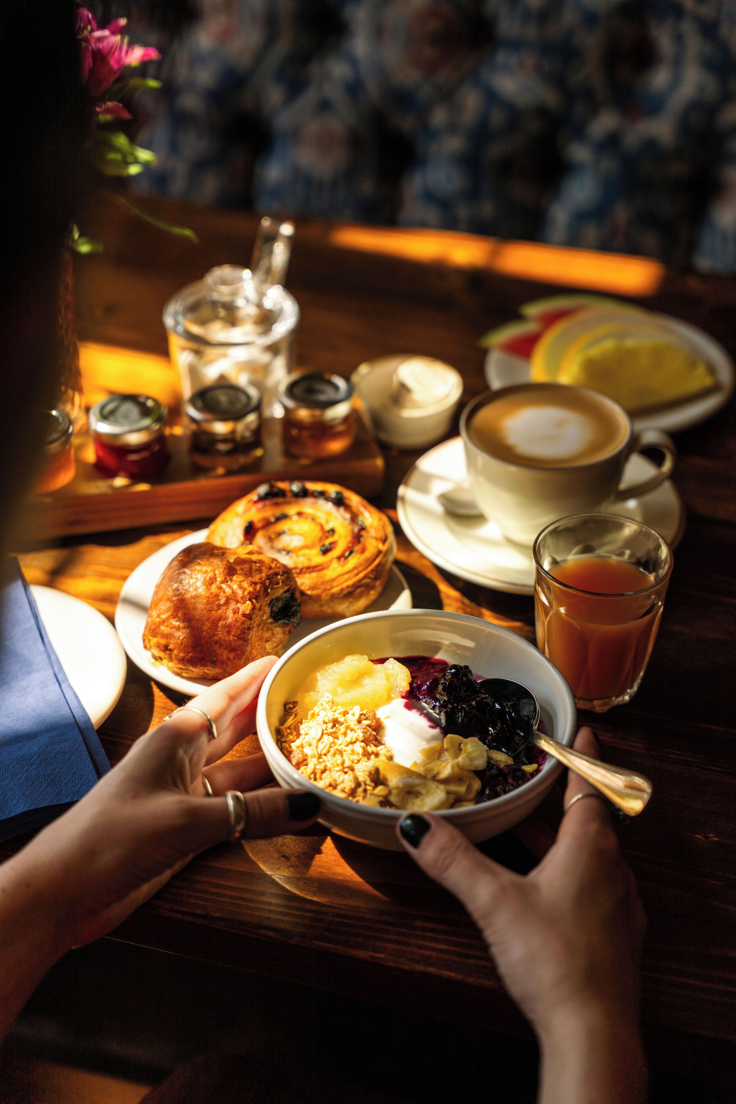 A breakfast setting with a variety of food items including pancakes, a bowl of cereal with fruit, a cup of coffee, and a glass of orange juice.