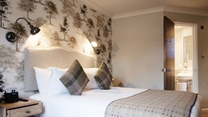 A neatly made bed with two pillows, a bedside table with a lamp, and a wall with a tree pattern. - The White Hart Hotel (Kingston Upon Thames)