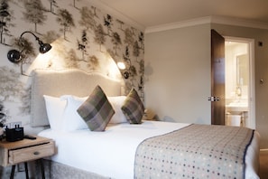 A neatly made bed with two pillows, a bedside table with a lamp, and a wall with a tree pattern.