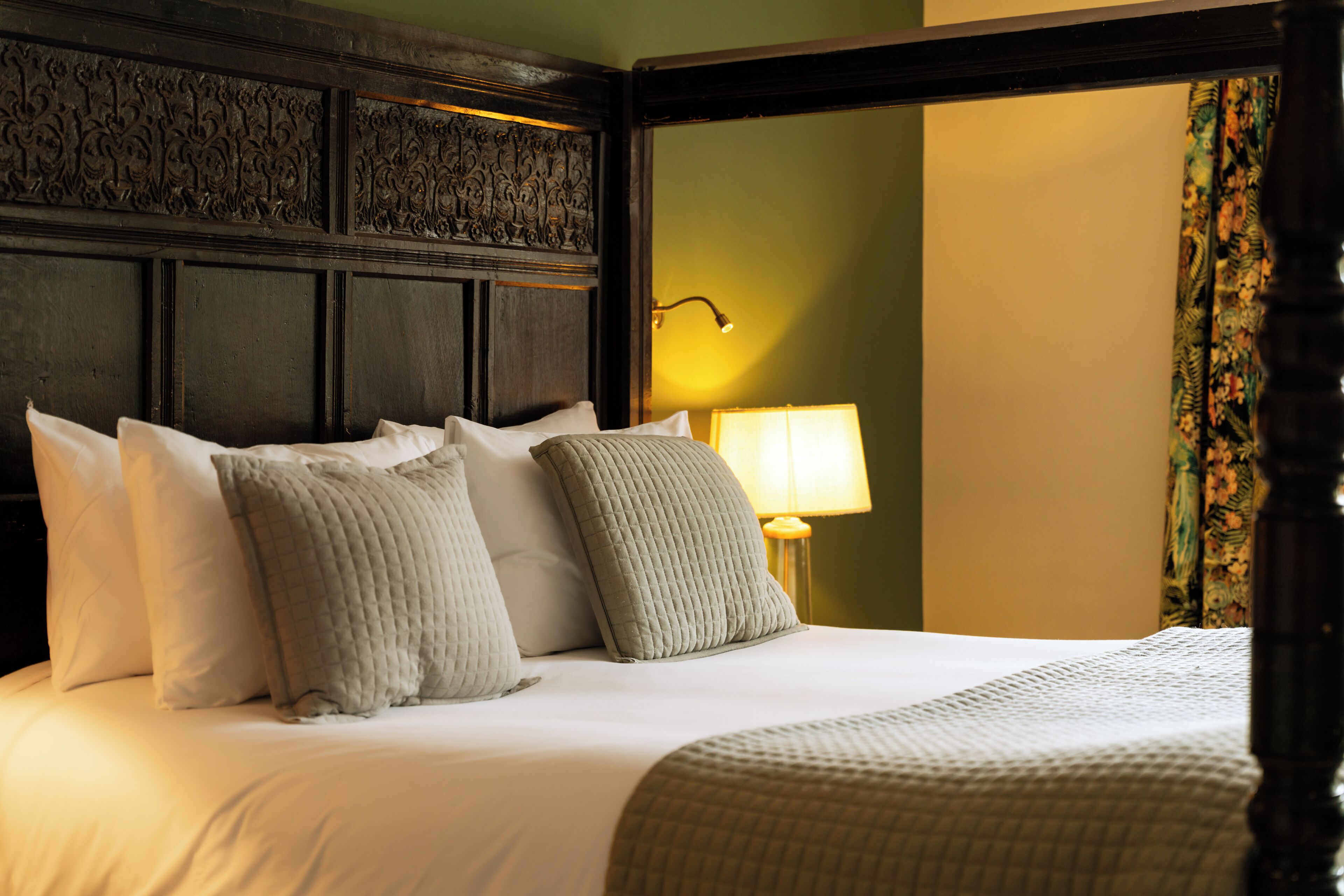 A bed with multiple pillows, a bedside lamp, and a headboard with intricate carvings.