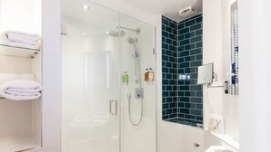 A modern bathroom with a glass-enclosed shower, white tiles, a wooden toilet, and a mirror with lights. - The White Hart Hotel (Kingston Upon Thames)