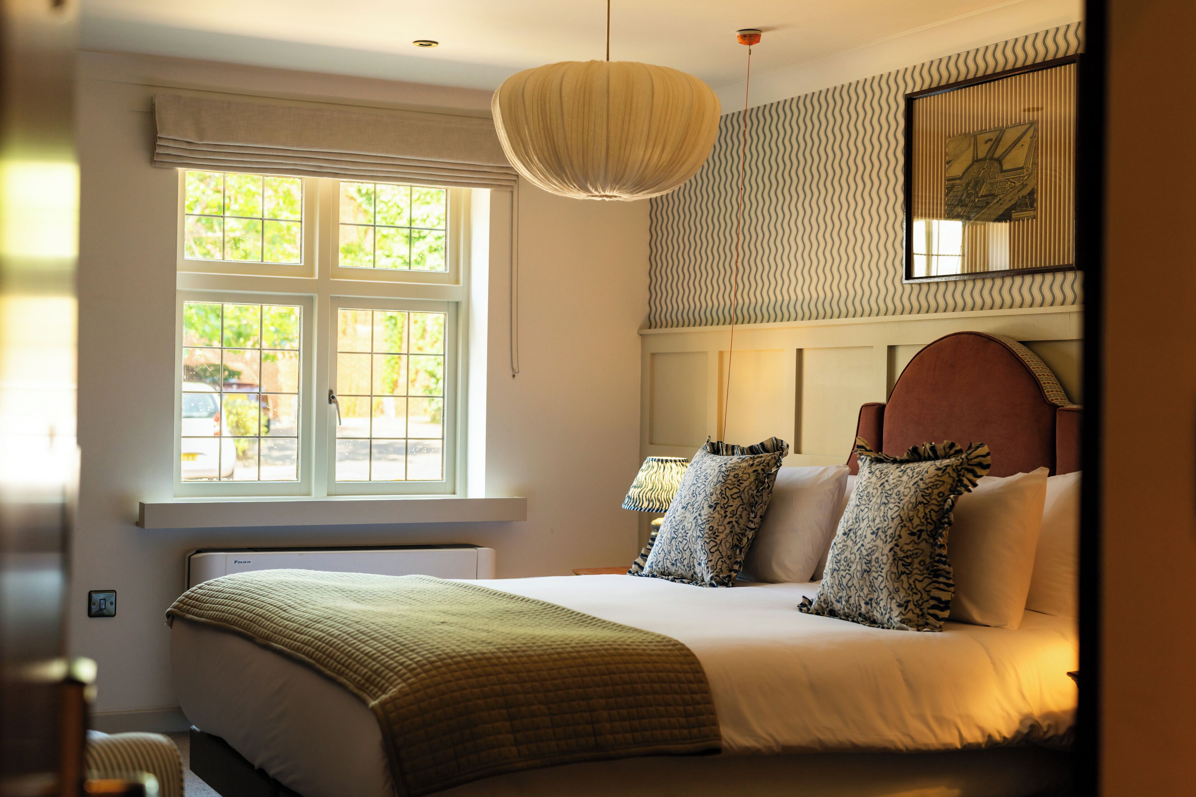 A bedroom with a bed, a window, a wall-mounted lamp, and a framed picture.