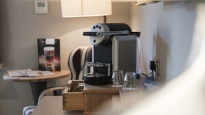 A coffee machine on a wooden table with two glasses and a coffee pod holder. - The White Hart Hotel (Kingston Upon Thames)