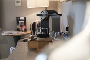 A coffee machine on a wooden table with two glasses and a coffee pod holder. - The White Hart Hotel (Kingston Upon Thames)