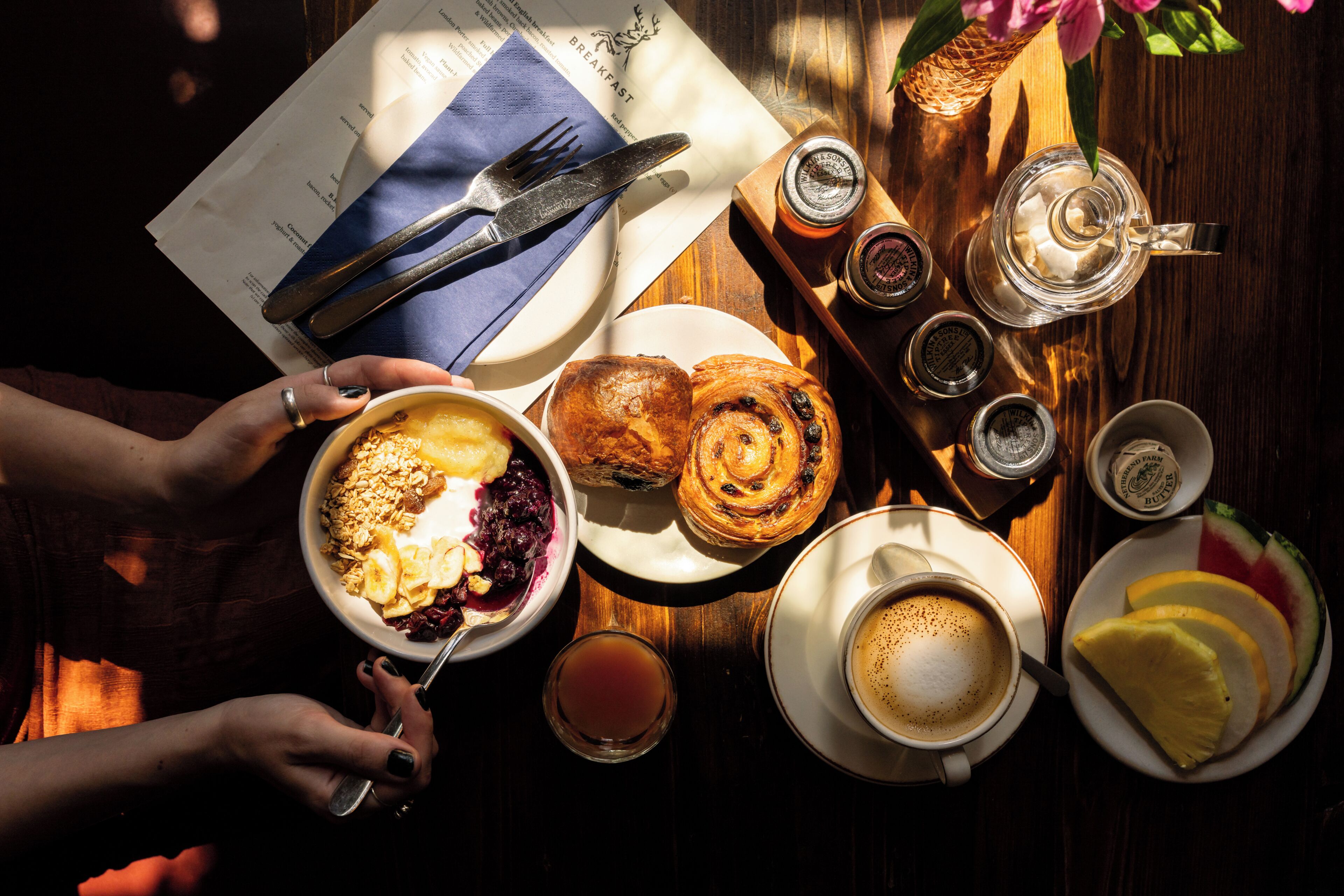 A breakfast setting with a variety of food items, including pastries, a bowl of cereal, and a cup of coffee.