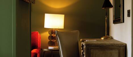 Una habitación con pared verde, una mesa de madera, una silla, un sillón rojo, una lámpara y un espejo.