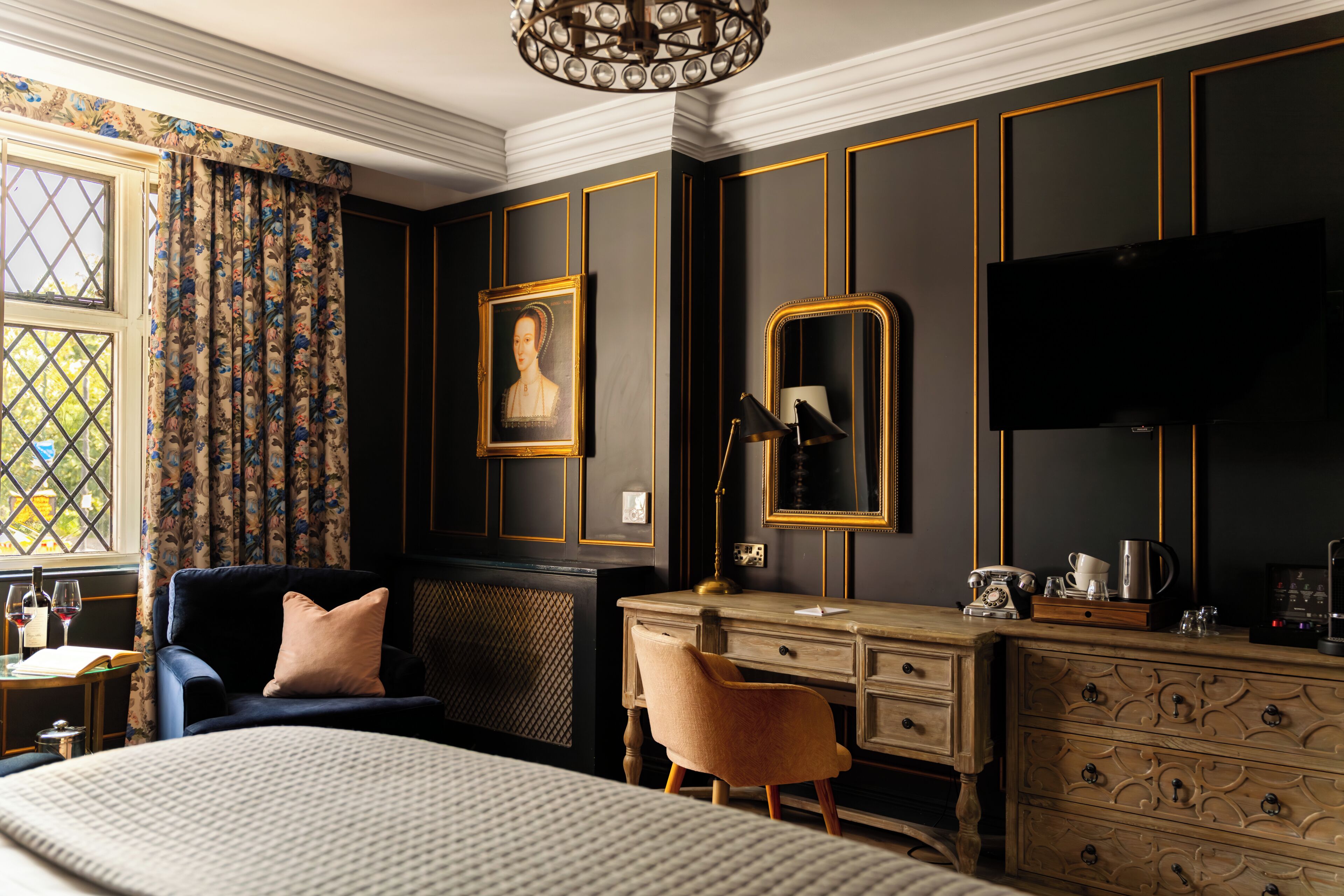 A room with a bed, a desk, a chair, a dresser, a mirror, a television, and a window with curtains.