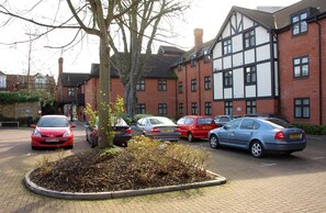 A parking area with several cars, a tree, and a building with a mix of brick and timber framing. - The White Hart Hotel (Kingston Upon Thames)
