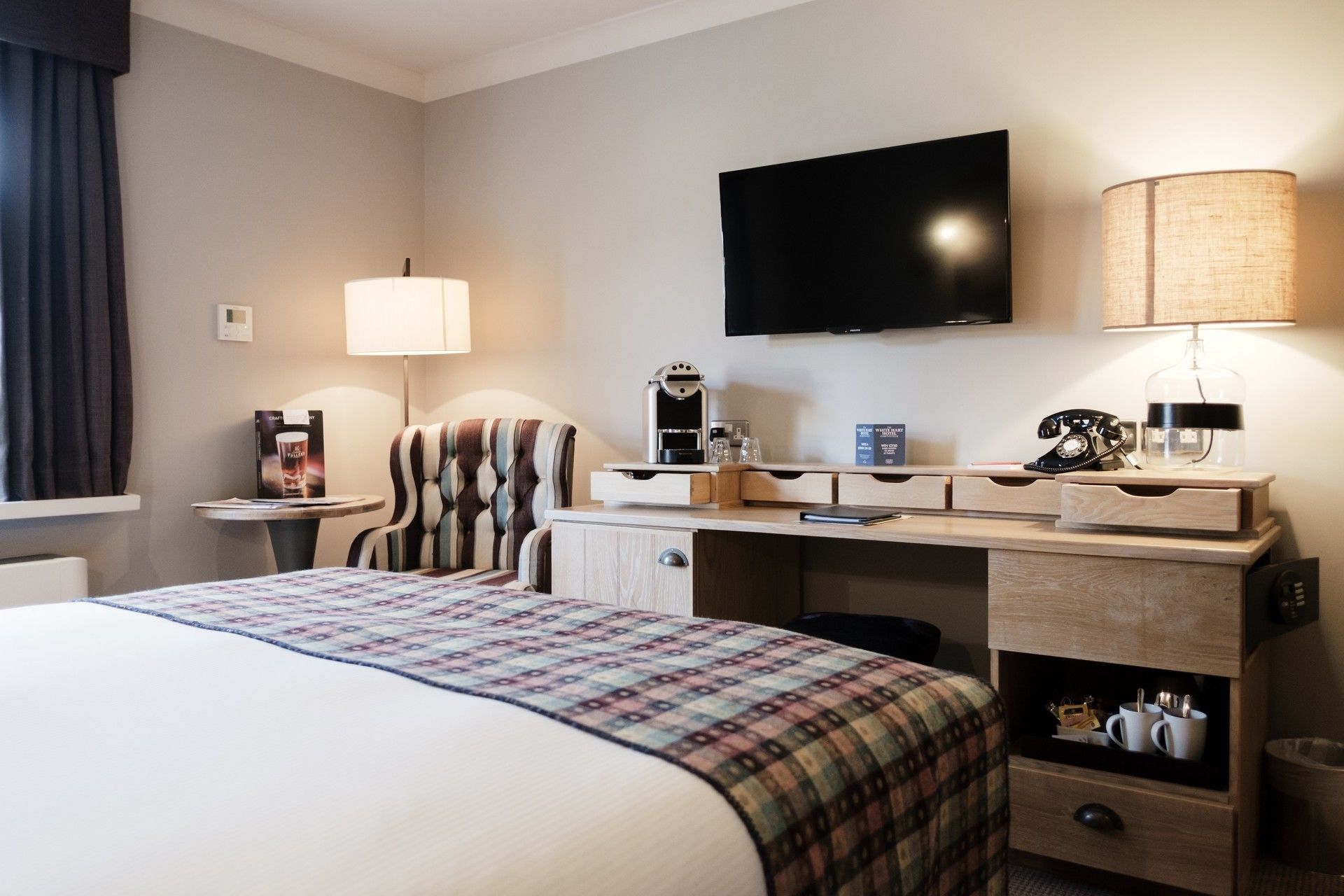 A hotel room with a bed, a desk with a lamp, a television, and a telephone.