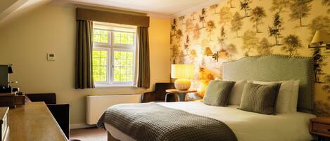 A hotel room with a large bed, a desk, a chair, a lamp, and a window with curtains.