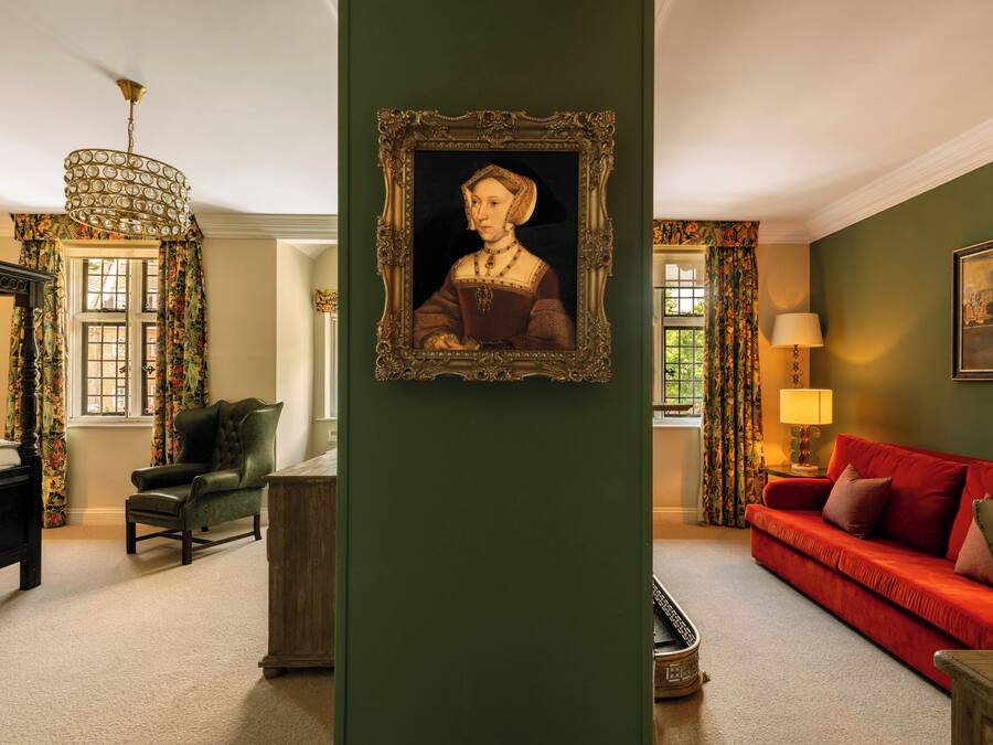 A room with a bed, a red sofa, a chair, a table, and a framed portrait on the wall.