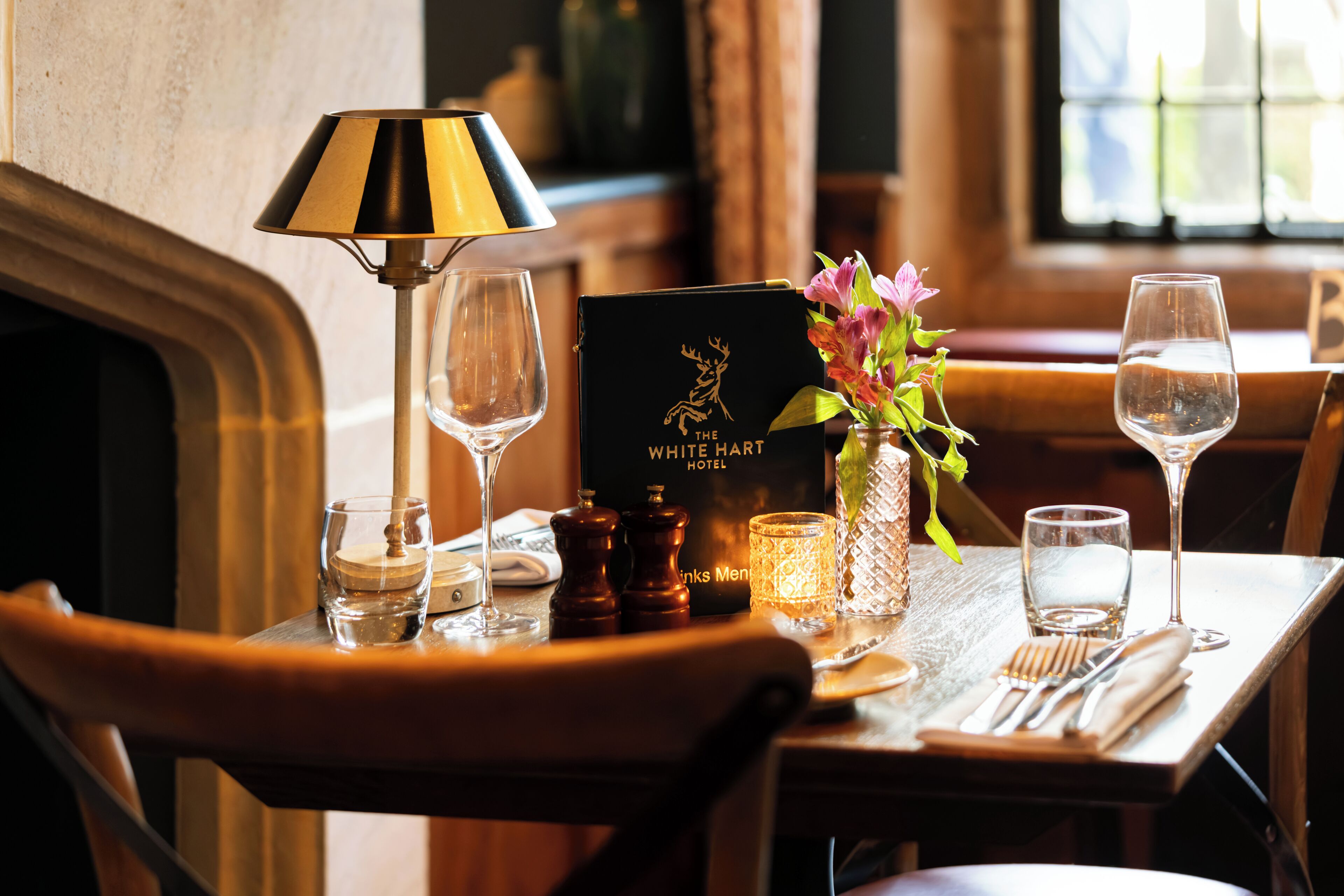 A dining table set with a wine glass, a candle, a menu, and a vase with flowers.