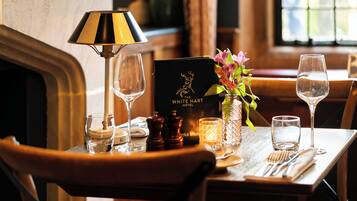 A dining table set with a wine glass, a candle, a menu, and a vase with flowers.
