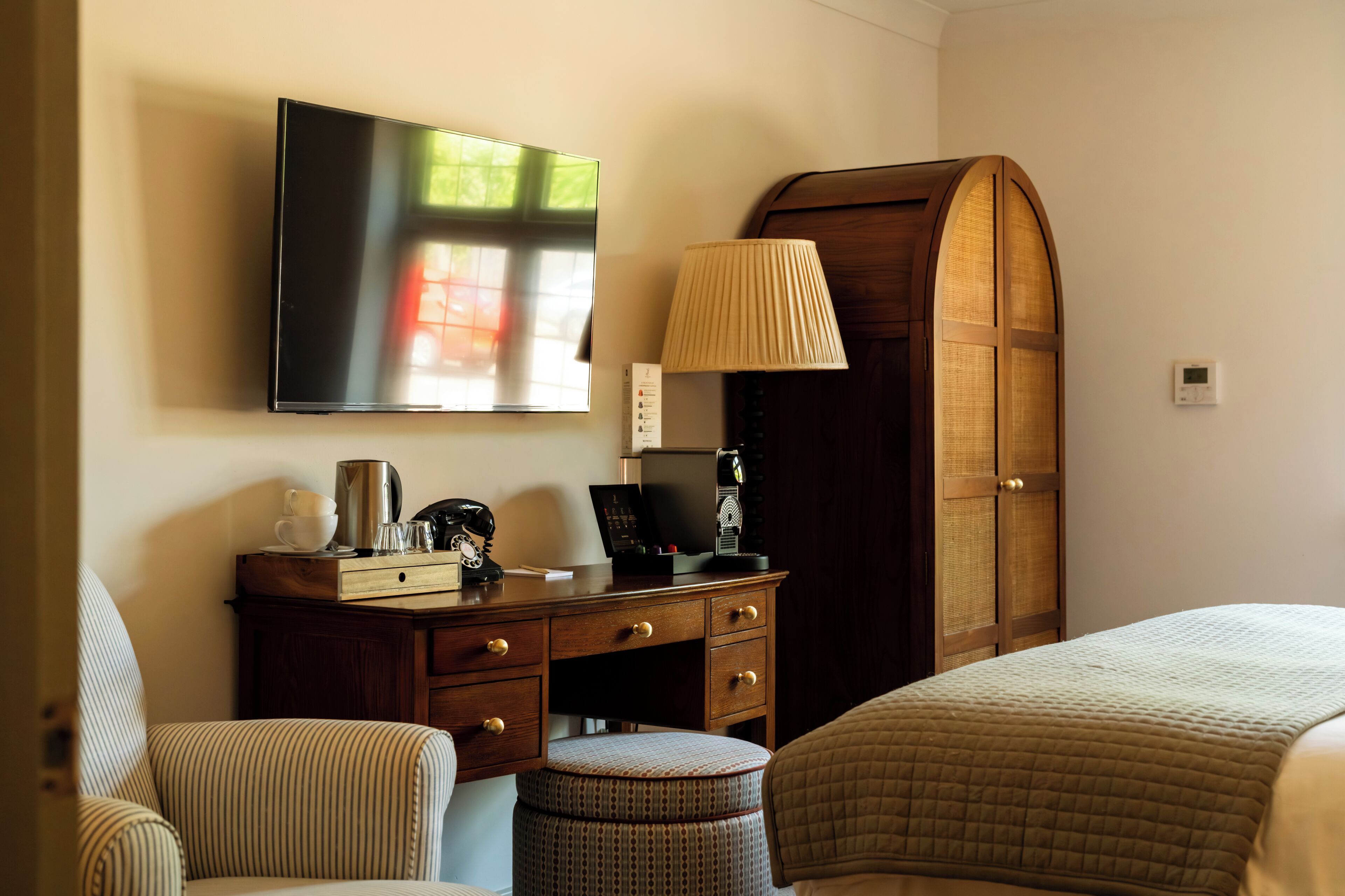 Una habitación de hotel con cama, escritorio con lámpara, televisor y armario.