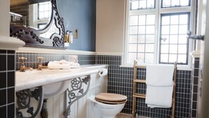 A bathroom with a white toilet, a sink with a mirror, and a window with a view of the outside. - The White Hart Hotel (Kingston Upon Thames)