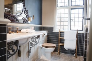 A bathroom with a white toilet, a sink with a mirror, and a window with a view of the outside. - The White Hart Hotel (Kingston Upon Thames)