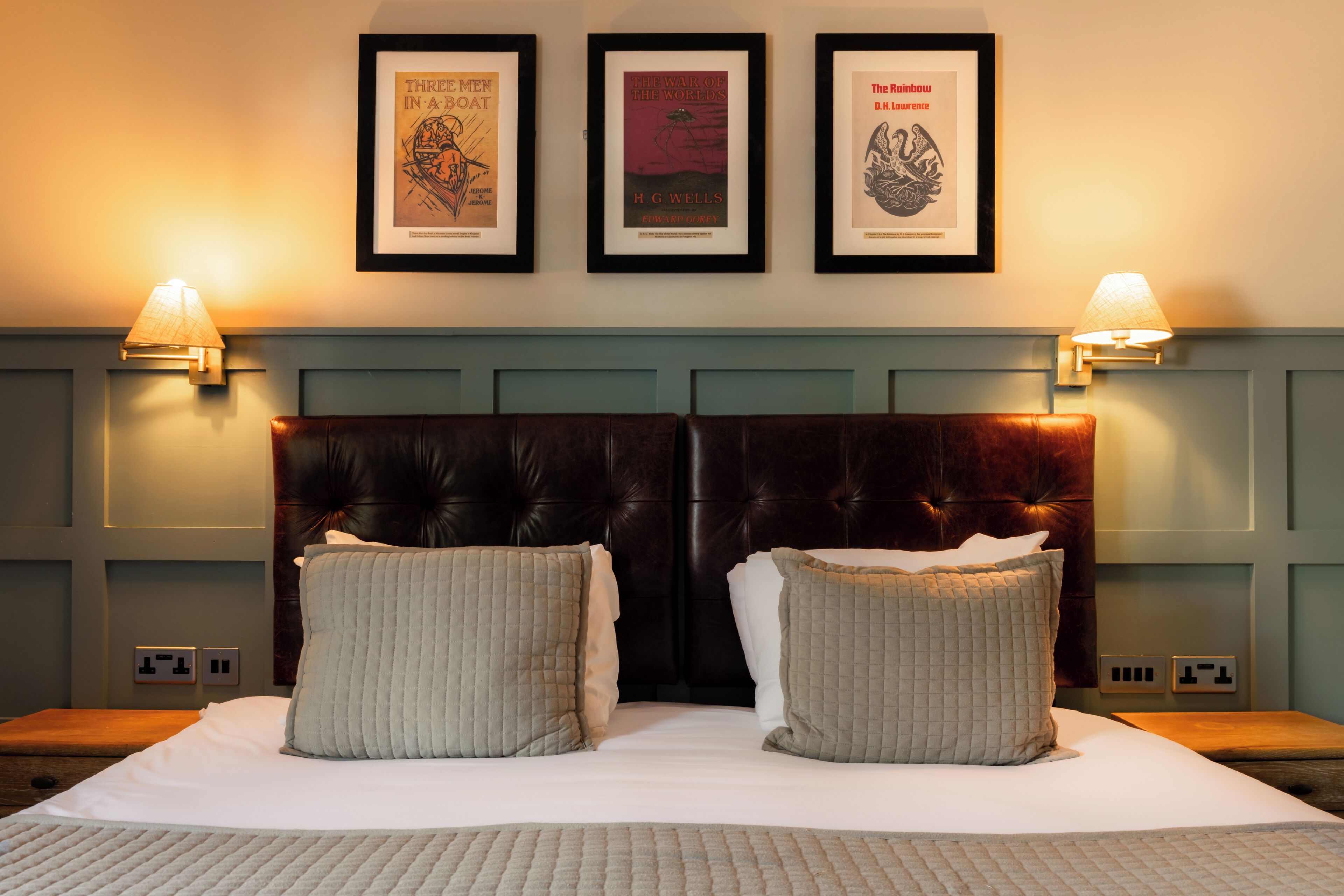 Une chambre d’hôtel avec un grand lit, deux lampes de chevet et trois livres encadrés accrochés au mur.