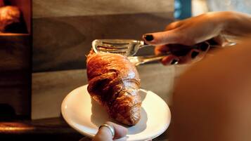 En person håller en croissant på en tallrik, och i bakgrunden syns en låda med croissanter.