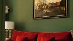 A room with a red sofa, a framed painting on the wall, and a lamp on a side table. - The White Hart Hotel (Kingston Upon Thames)
