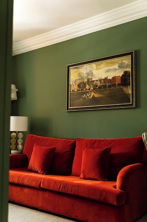 A room with a red sofa, a framed painting on the wall, and a lamp on a side table.