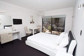 A modern hotel room with a large bed, a desk, a chair, a television, and a view of the outdoors.