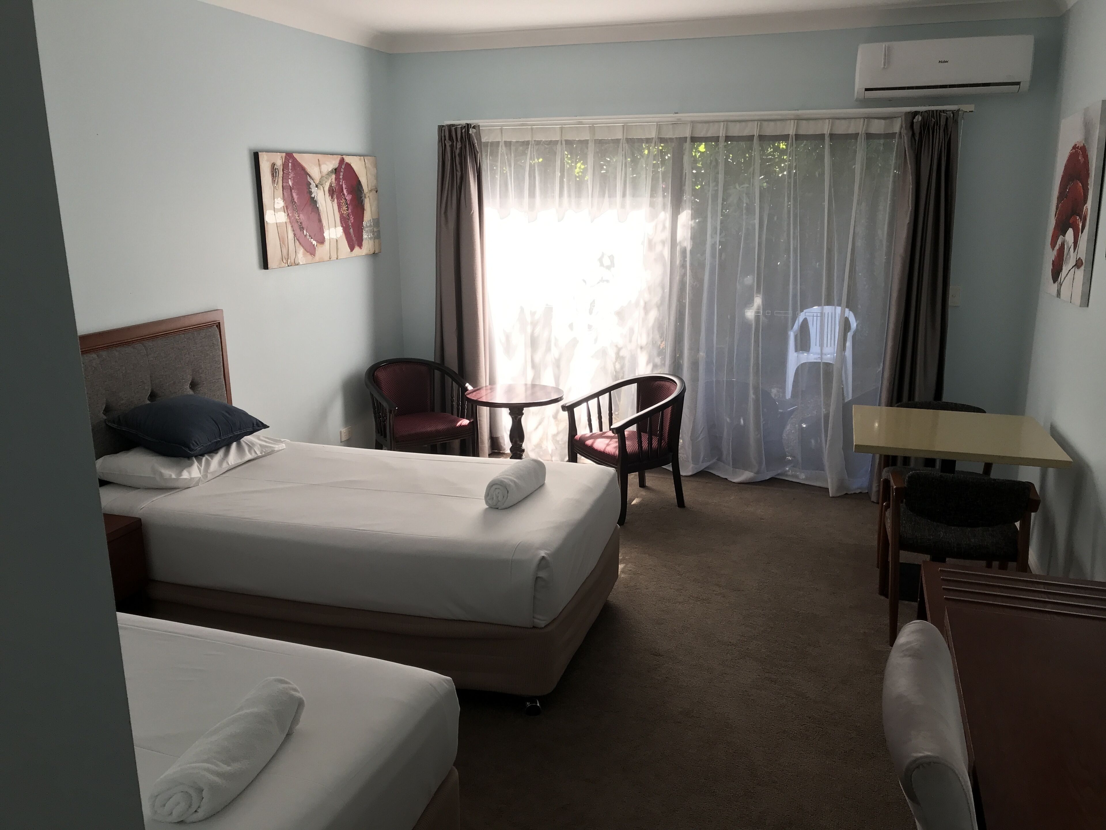 Une chambre d’hôtel avec deux lits, un bureau, une chaise et une fenêtre avec des rideaux.