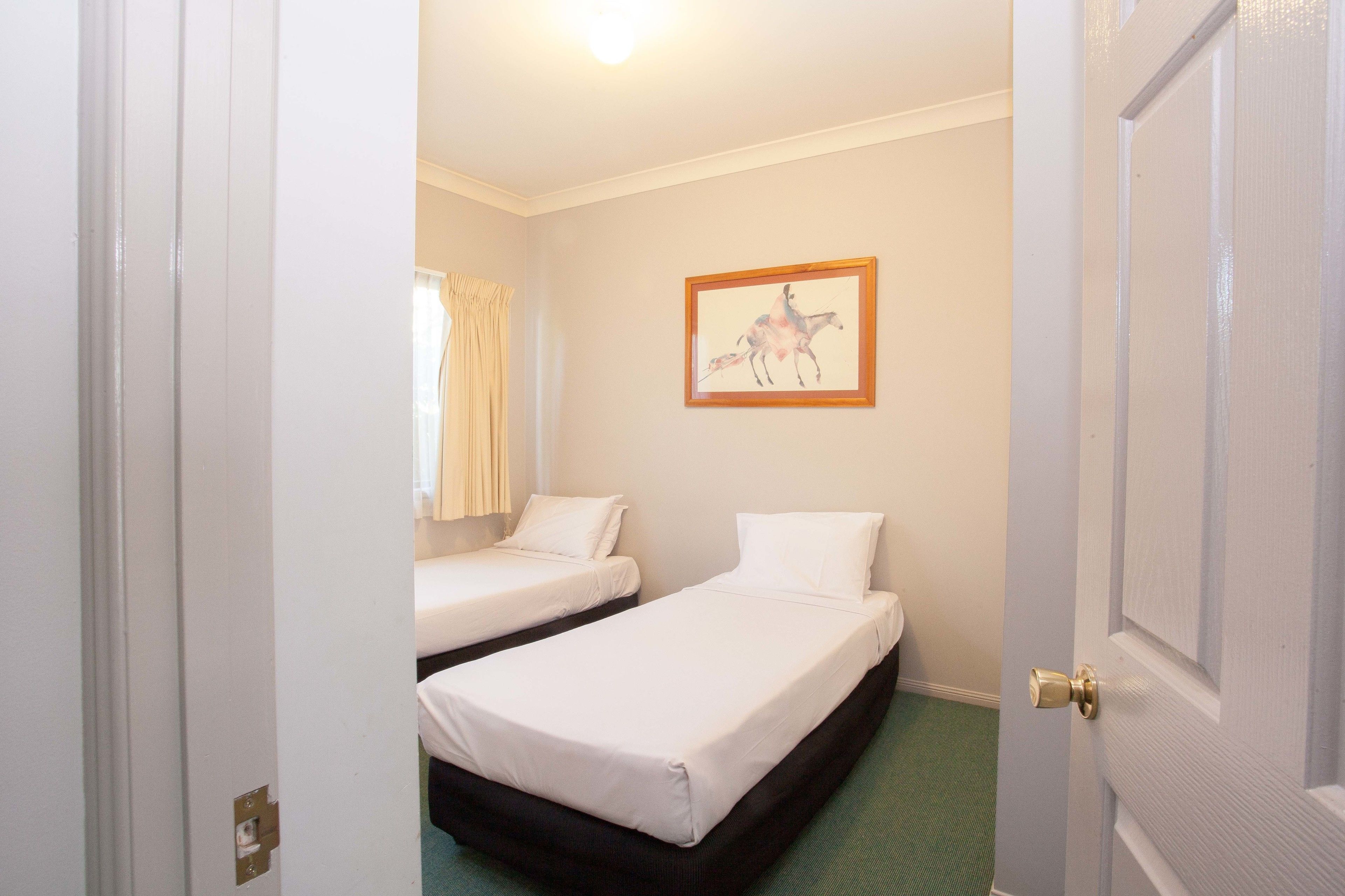 Ein Hotelzimmer mit zwei Einzelbetten, einem gerahmten Bild an der Wand und einer Tür mit Messinggriffen.