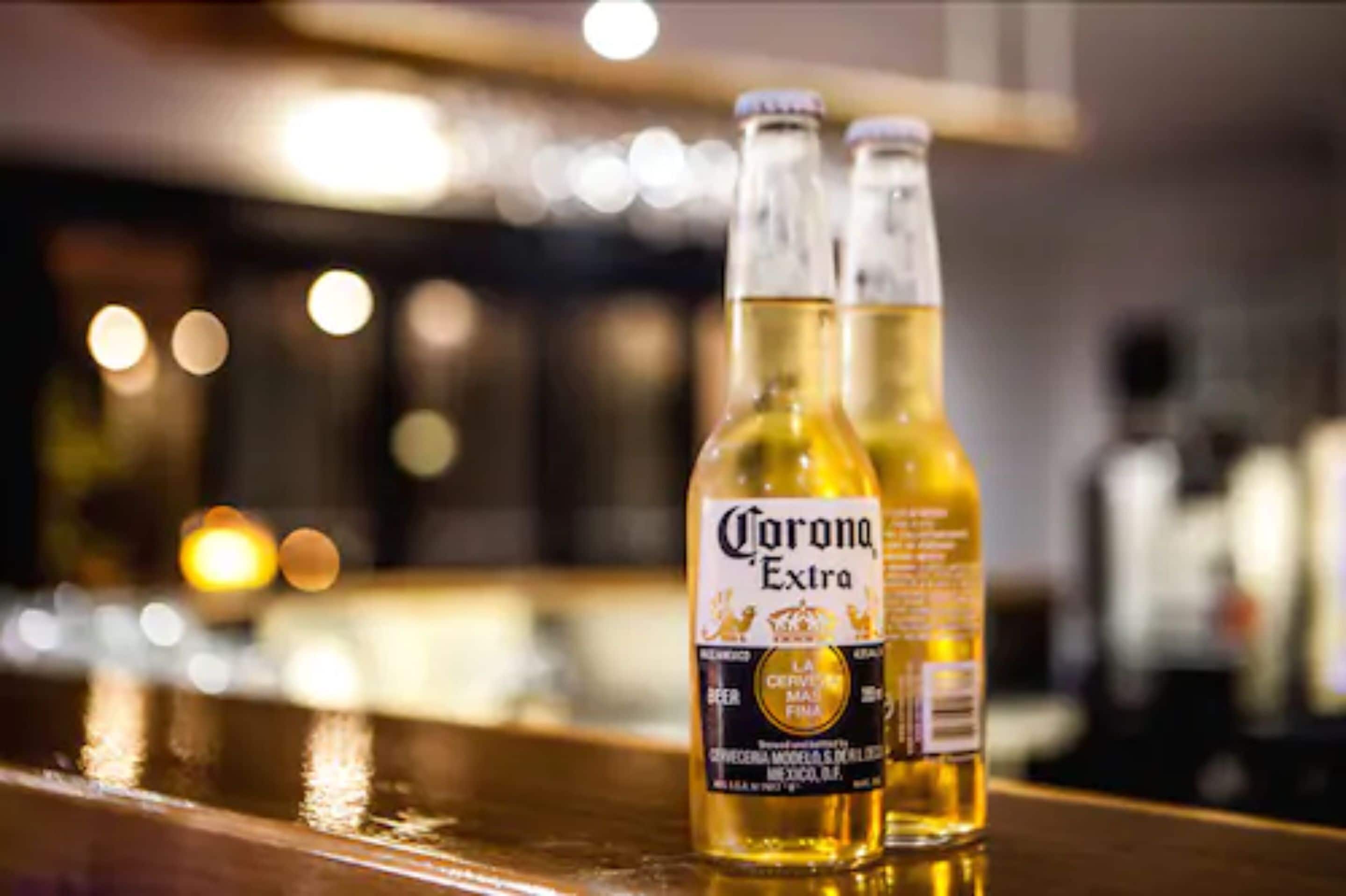 Two bottles of Corona Extra beer on a bar counter with a blurred background.