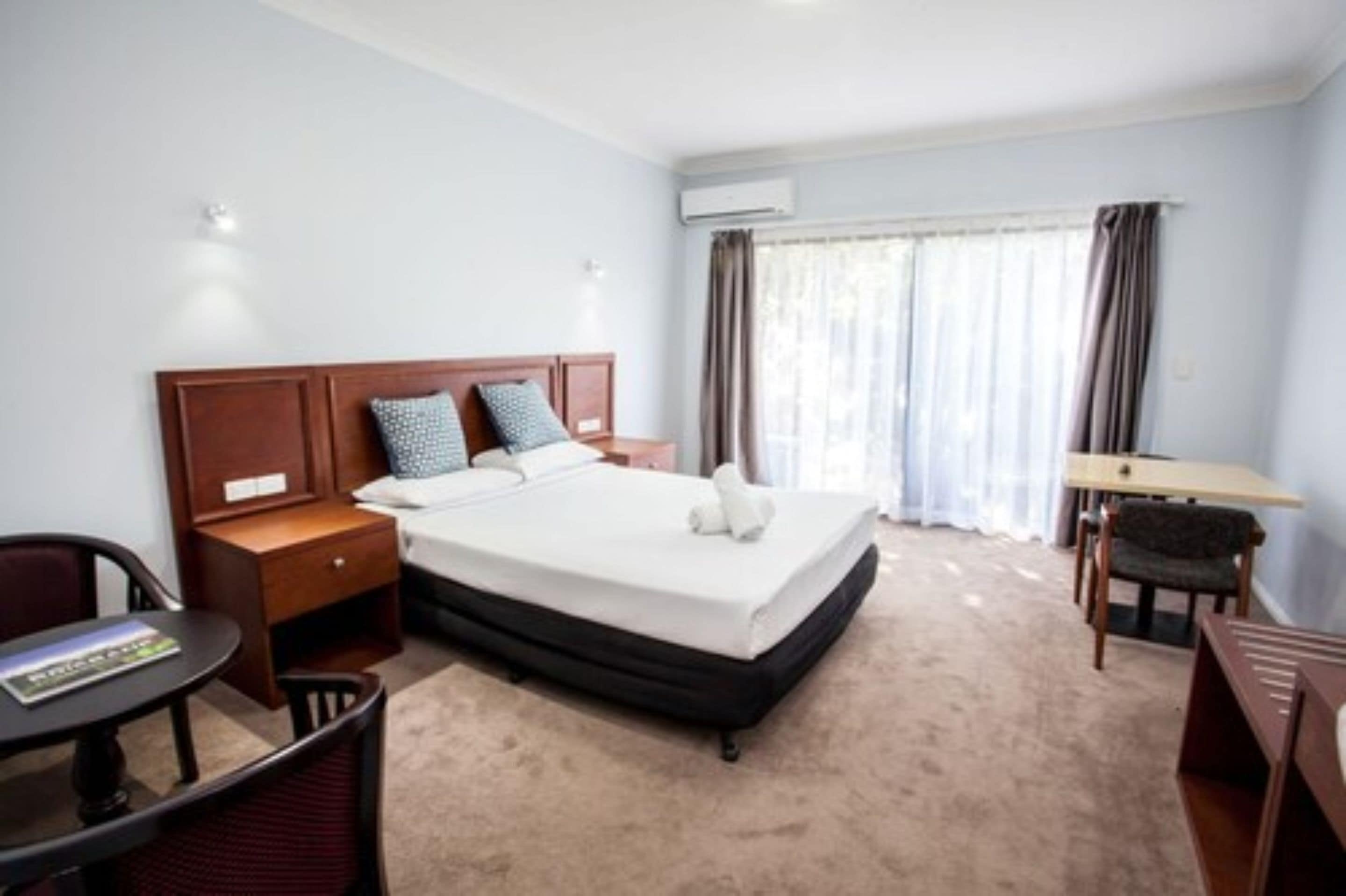 Una habitación de hotel con cama, mesita de noche, silla, escritorio y ventana con cortinas.
