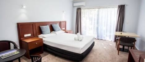 Una habitación de hotel con cama, mesita de noche, silla, escritorio y ventana con cortinas.