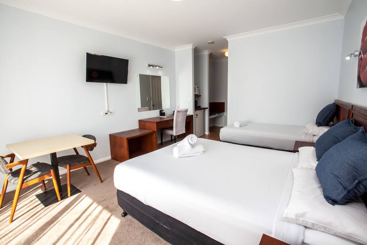 Quarto de hotel com cama, escrivaninha, cadeira, televisão e banheiro.