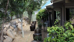 Un jardín con rocas grandes, plantas en macetas y un edificio de techo azul.