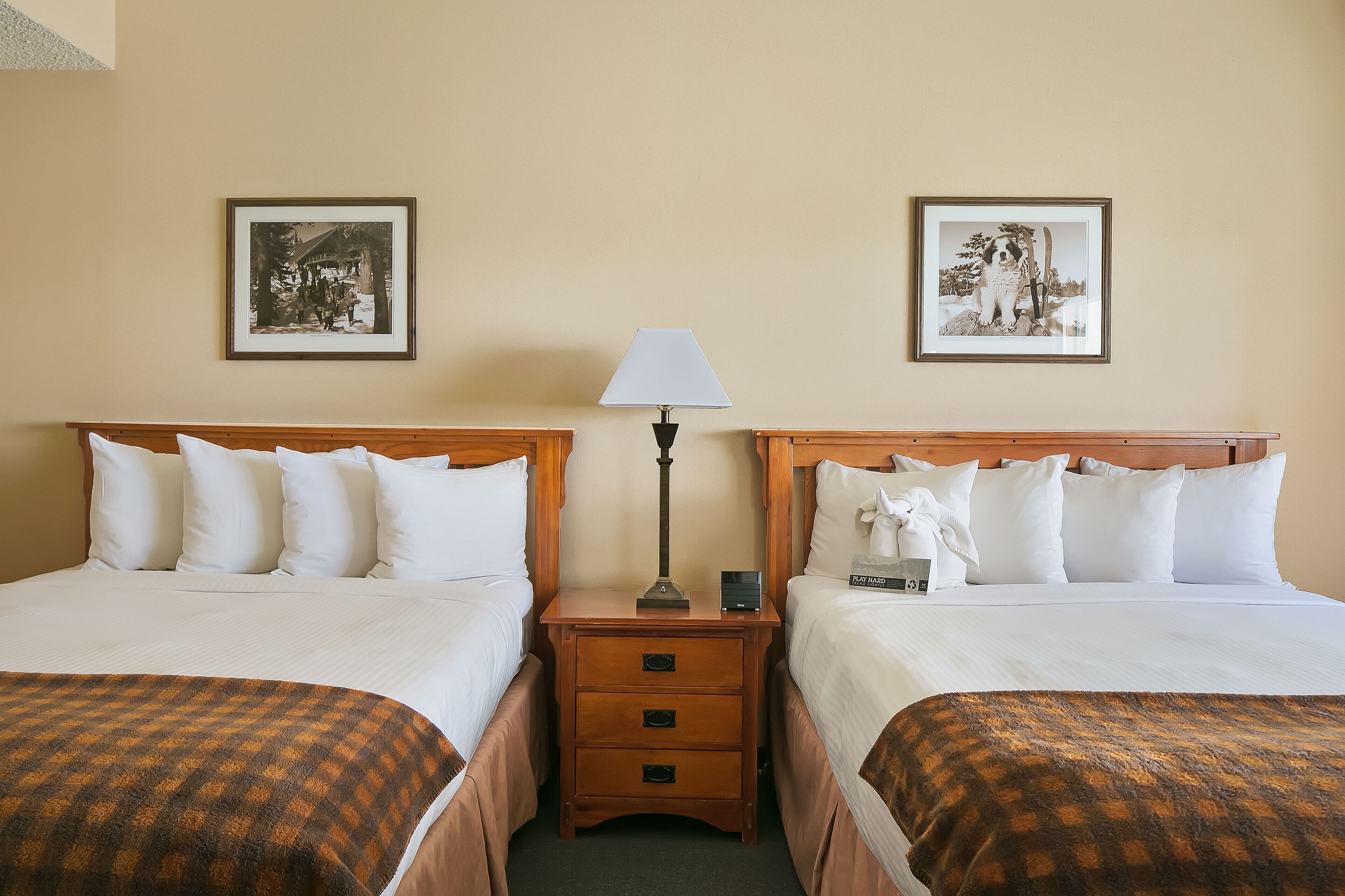 A hotel room with two beds, a nightstand with a lamp, and two framed pictures on the wall.