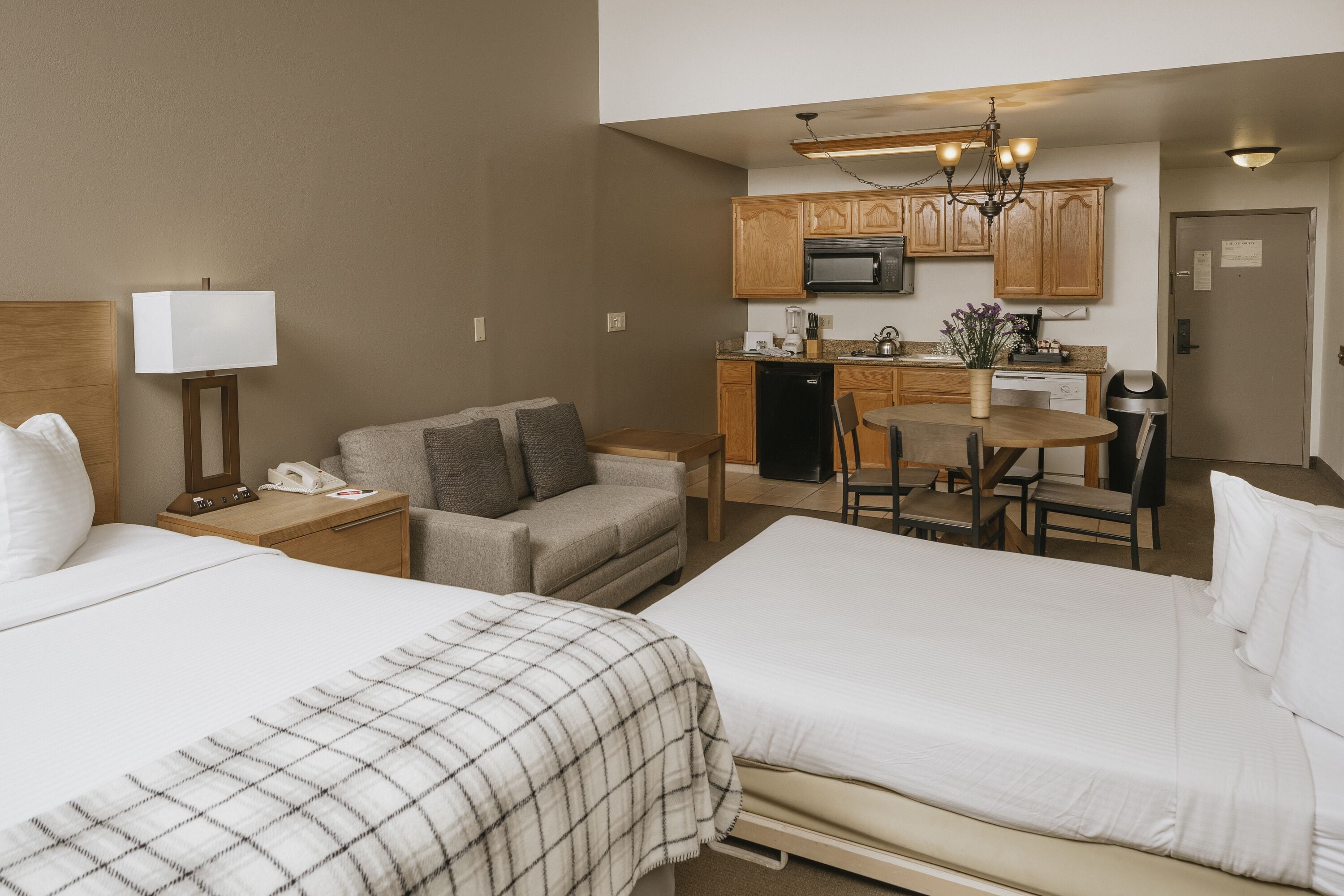 Habitación de hotel con dos camas, un sofá, una pequeña cocina equipada con microondas y una mesa de comedor.