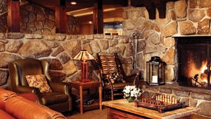 A cozy lounge area with a stone wall, a fireplace, leather seating, and a chess table.