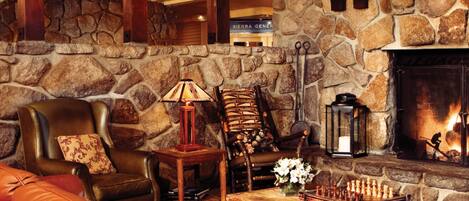 A cozy lounge area with a stone wall, a fireplace, leather seating, and a chess table.