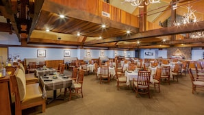 A spacious dining area with multiple tables and chairs, wooden beams on the ceiling, and a chandelier.
